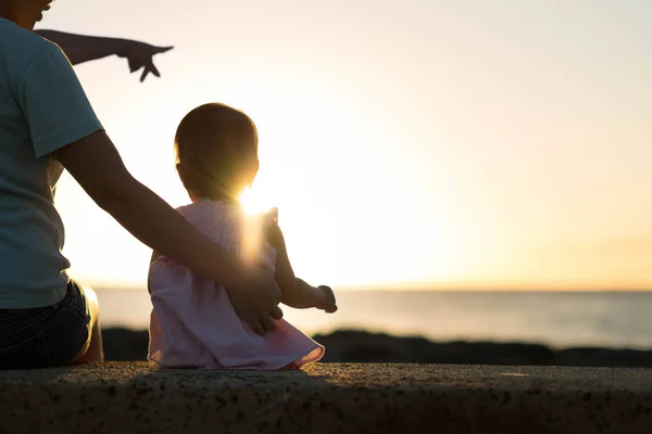 Mãe e criança sentados juntos na praia, observando o belo pôr do sol . — Fotografia de Stock