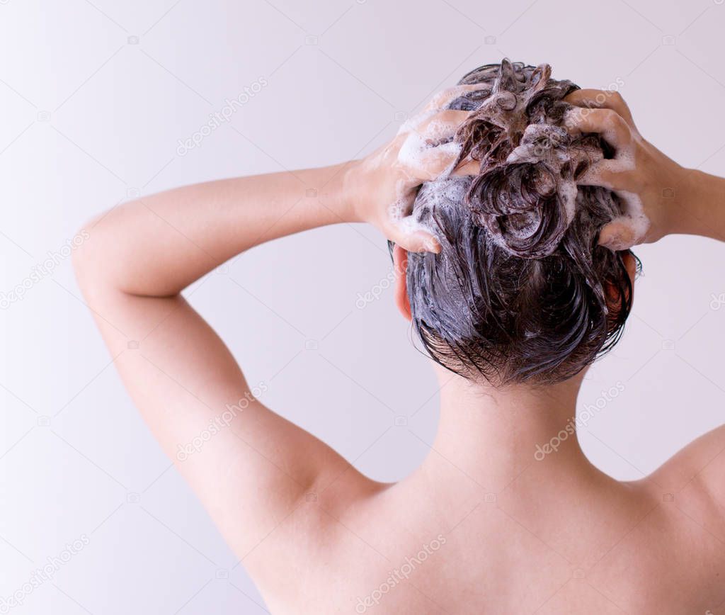 Woman shampoos hair close up with both hands on a white background