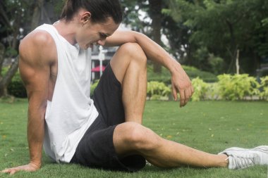 Parktaki çimlerin üzerinde oturan adam hareketli bir kardiyo çalışmasından sonra mola veriyor..