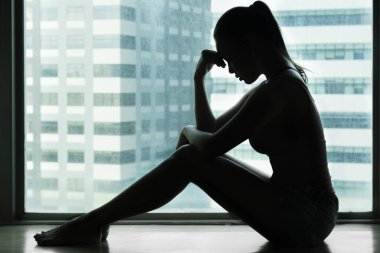 Şehrin arka planında, penceresinin yanında oturan üzgün bir kadının silueti..