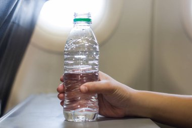Uçak uçuşunda plastik bir şişeyi suyun üzerinde tutan bir kadın el. Su ve plastik kirliliği.