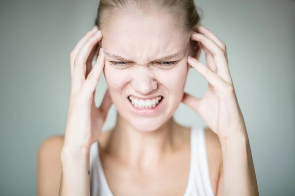 A mad woman going crazy from her surroundings and loud sounds, hands on her face trying to clear her head.