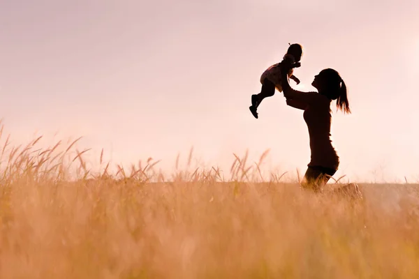 Mama Podnosząc Swoje Dziecko Powietrzu Bawiąc Się Siedząc Miękkiej Trawie — Zdjęcie stockowe