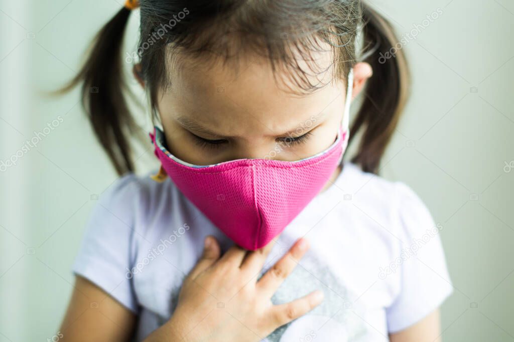 Little asian girl suffering from dirty air pollution, holding her chest wearing a protective mask outside.