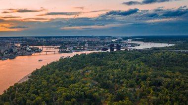 Dniepr nehrinin üzerinde inşaatı devam eden bir köprüsü olan Skyline. Kyiv (Kiev) şehrinde yaz mevsiminde gün batımının insansız hava aracı ile hava görüntüsü çekilir..