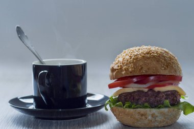 Bir fincan sıcak kahve gri bir arka plan üzerinde hamburger