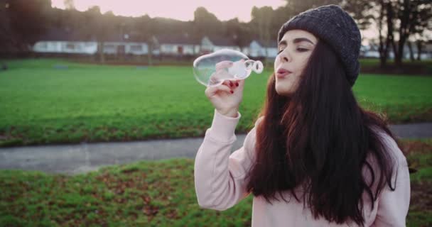 Красивая белая девушка с длинными кудрявыми волосами пускает пузыри днем . — стоковое видео