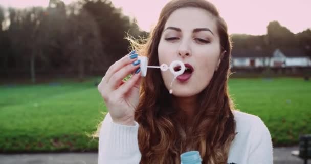 Young attractive brunette blowing bubble in the park, slow motion. — Stock Video