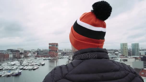 Человек в специальной цветной шляпе, стоящий на барьере на крыше. 4k — стоковое видео