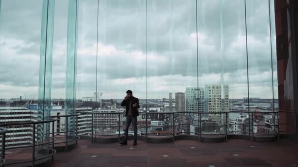 Een man uit een wolkenkrabber met uitzicht op de skyline van de stad, silhouet, praten over de telefoon en dan dansen. In een onderhoudende manier. 4k — Stockvideo