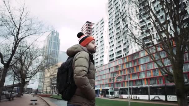 Um turista masculino com um chapéu colorido, olhando para longe. Cidade desenvolvida. 4K. Plano geral . — Vídeo de Stock