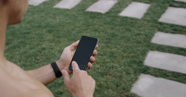 Corredor de los hombres que sostienen el teléfono inteligente utilizando la pantalla táctil para elegir el ejercicio en la aplicación antes de correr en pista. Video cámara lenta 4k . — Vídeo de stock