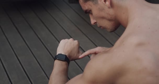 Un joven mira el reloj y hace ejercicios. 4k — Vídeo de stock