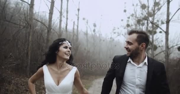 Happy newlyweds run holding hands ,and look at each other through forest 4k — Stock Video