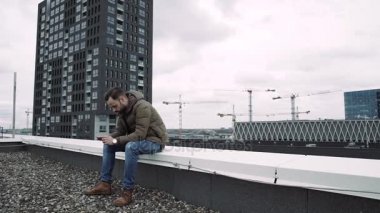 Genç çocuk, elinde telefon ile çatı üzerinde duran bir ileti yazın. Ağır çekim. 4k