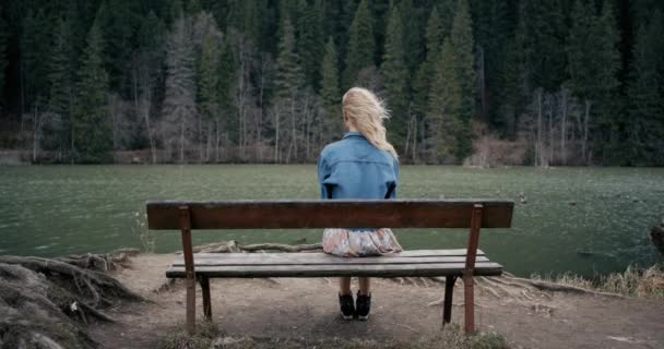 La jeune femme repose sur un banc au bord du golfe. Les cheveux longs volent sur le vent frais. Sur la rive du lac. 4k — Video