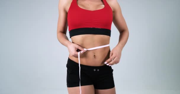 Chica atlética joven en la parte superior de fitness y pantalones cortos que miden la cintura con cinta métrica. 4k. La epopeya roja. Moción lenta — Vídeo de stock