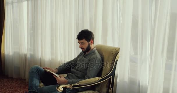 Человек читает в роскошном гостиничном номере. Ветер стучит в окно. 4k — стоковое видео