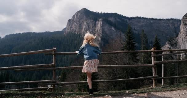 Jovem fêmea de pé na beira do penhasco e levantando as mãos contra altas montanhas rochosas. Menina feliz desfrutando de sucesso e vista deslumbrante . — Vídeo de Stock