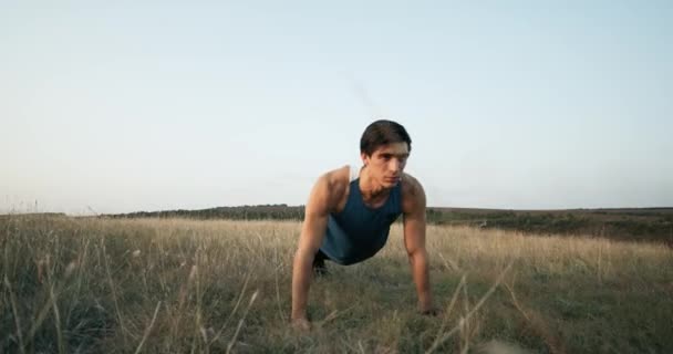 Een knappe man in trendy outfit maakt push ups tijdens de video. Hij draagt een blauw T-shirt. Het mannetje is trainen in het park. Slow-Motion. 4k — Stockvideo