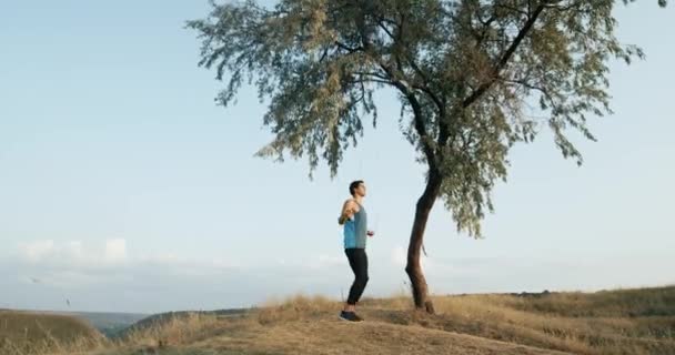 Guy jumps on a skipping rope on a dry meadow. Guy engaged in sports. Man doing sports a workout on a skipping rope. 4k — Stock Video