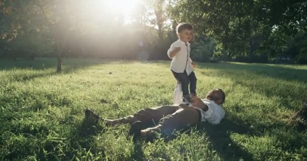 Der junge Vater und sein kleiner Sohn spielen auf dem Hinterhof. sie liegen zusammen auf dem Rasen.