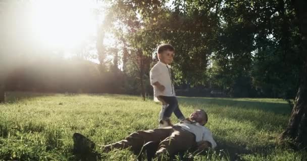 Der junge Vater und sein kleiner Sohn spielen auf dem Hinterhof. Sie liegen zusammen auf dem Rasen. Sonnenuntergang über dem Hintergrund