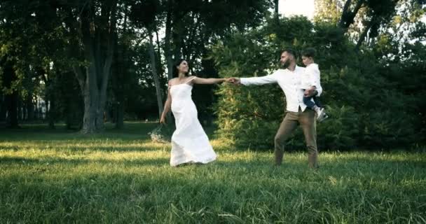 Familia joven: padres jugando con su hijo pequeño. La esposa tira de su mano maridos, sonriendo al aire libre en un día soleado. Feliz infancia y concepto de paternidad . — Vídeos de Stock