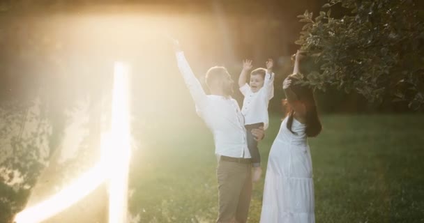 Ung familj:. Glad mamma och pappa kramar sin baby, ler utomhus en solig dag. Lycklig barndom och föräldraskap koncept. Solljus i linsen. — Stockvideo