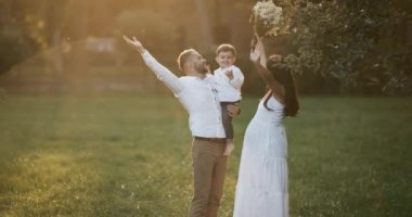 Genç aile: toddler oğulları ile oynarken anne. Mutlu anne ve baba bebeklerini açık havada gülümseyen güneşli bir günde, sarılma. Mutlu çocukluk ve ebeveynlik kavramı. Güneş ışığı objektif