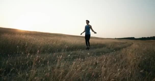 Un joven en un traje deportivo que hace ejercicios en una cuerda para la resistencia amasada en la naturaleza en la montaña, el atleta salta para fortalecer los músculos . — Vídeo de stock