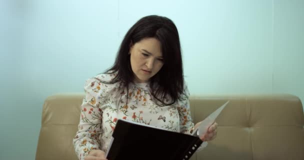 Mujer se sienta en el sofá y la lectura del contrato — Vídeo de stock