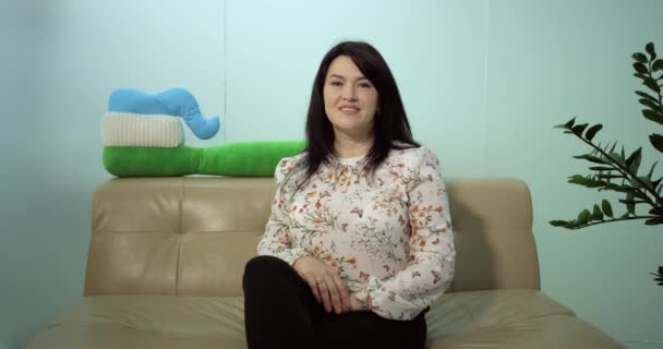 Woman sits alone on sofa in a waiting area , happy and smiling waiting for her check appointment — Stock Video