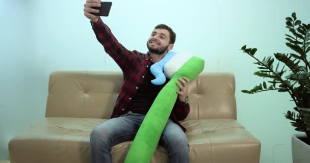 Sorrindo homem tirar uma selfie com uma escova de dentes sentado no sofá — Vídeo de Stock