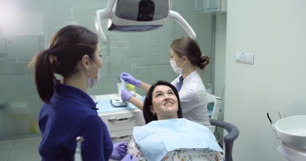 Dentista fazer um check-up e limpeza dental para uma jovem mulher, enfermeira dentária estão ao lado — Vídeo de Stock