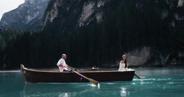 Adam kürek, birlikte vakit ahşap tekne arka plan bir göl ortasında inanılmaz romantik çift şaşırtıcı dağlar vardır. Kırmızı epik