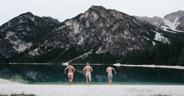 Paisaje perfecto en medio de montañas con un gran lago tres jóvenes corren hacia el lago y saltan al agua. 4k. EPIC rojo. Moción lenta — Vídeos de Stock