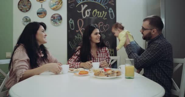 Mañana en la cocina una familia feliz tomando el desayuno, mamá y papá están jugando con su bebé — Vídeo de stock