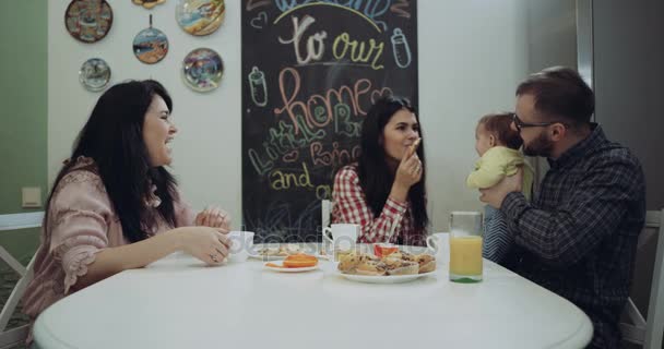 Familia feliz sentada en la mesa de la cocina tomando vrea y jugando con el bebé. 4k. épica roja — Vídeo de stock