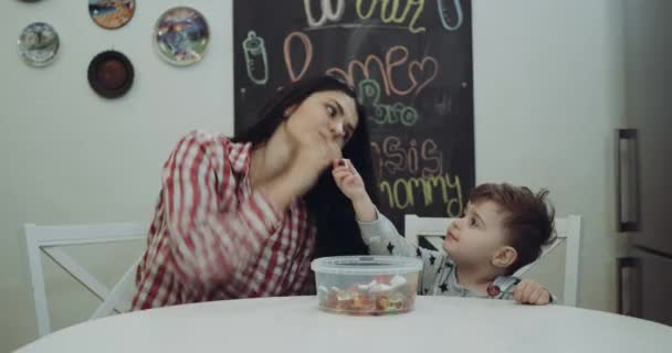 Молодая женщина со своим мальчиком сидит за кухонным столом и играет вместе с желе, счастливо провести время — стоковое видео