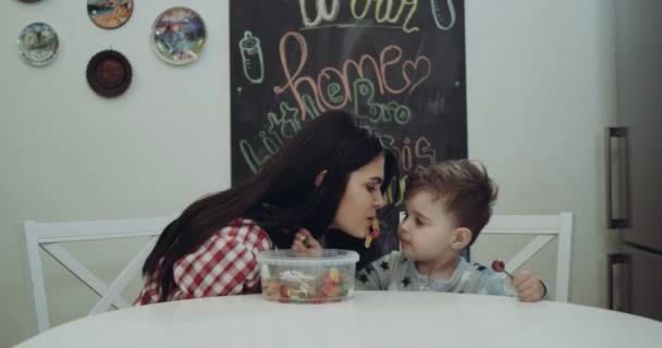 Mãe feliz e seu filho sentado na cadeira da cozinha comendo doces — Vídeo de Stock