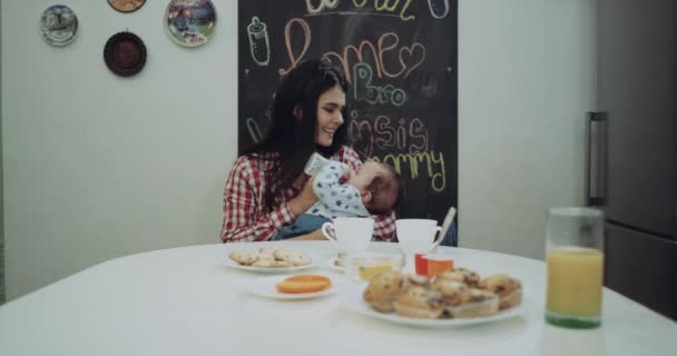 Молода мати дає їжу своєму маленькому хлопчикові за кухонним столом — стокове відео
