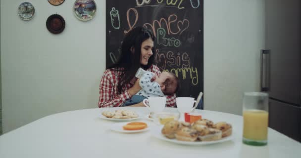 Joven madre dando la comida para su bebé en la mesa de la cocina — Vídeos de Stock