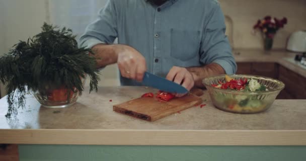 Närbild ung man skär grönsaker i köket. — Stockvideo