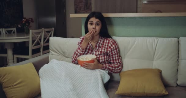 Mujer joven viendo la televisión comiendo las palomitas de maíz y está muy emocionada . — Vídeo de stock