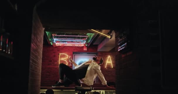 Charismatische jonge mannen met zwarte baard is vrolijk op de bar tafel mooi tijd doorbrengen op het donkere café met verbazingwekkende lichten. — Stockvideo