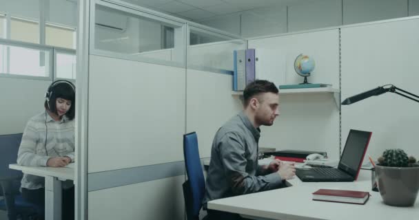 A Hivatal és a fiatal férfi és a nő ül a Hivatal asztal dolgozik a laptop a tipikus munkanap. — Stock videók