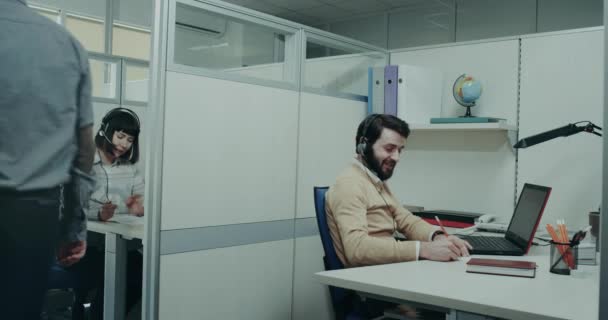 En el centro de llamadas, el trabajador carismático que habla con el cliente usando los auriculares feliz y sonriente toma notas. épica roja — Vídeos de Stock