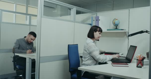 Робочий день в офісі, молодий чоловік і жінка, сидячи на столі, працюють зосереджено, молода жінка розмовляє зі своїм колегою, запитуючи щось. 4k — стокове відео