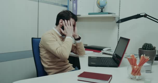 Journée de travail acharnée au bureau, jeunes hommes assis sur sa table et regardant nerveusement à travers l'ordinateur portable — Video